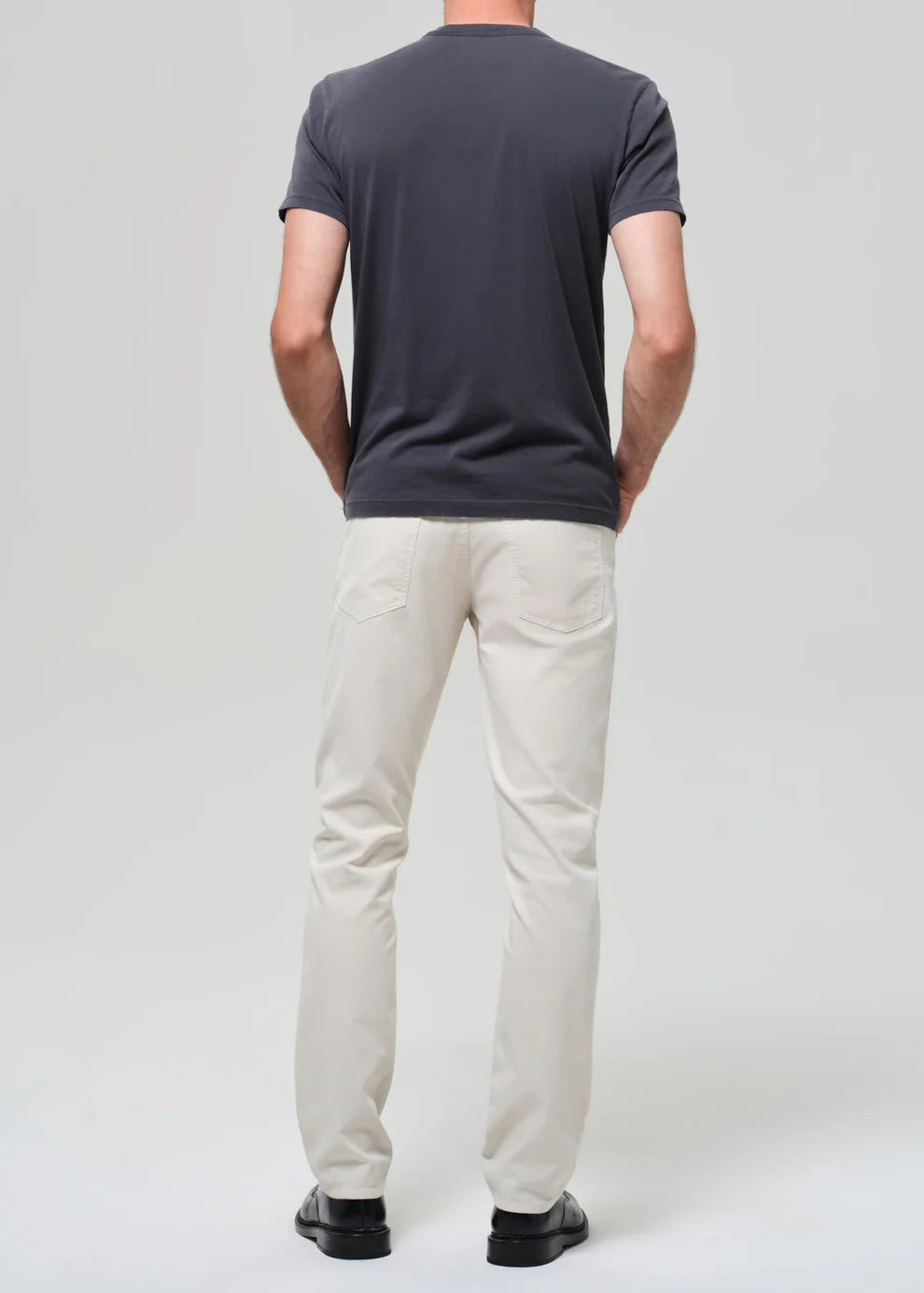 Person wearing a dark gray t-shirt and light beige pants on a white background
