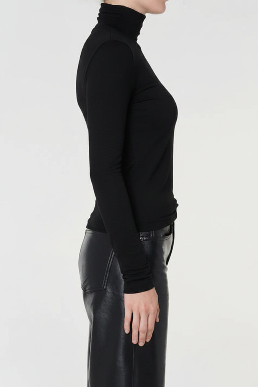 Person wearing a dark gray turtleneck sweater and black leather pants on a light gray background