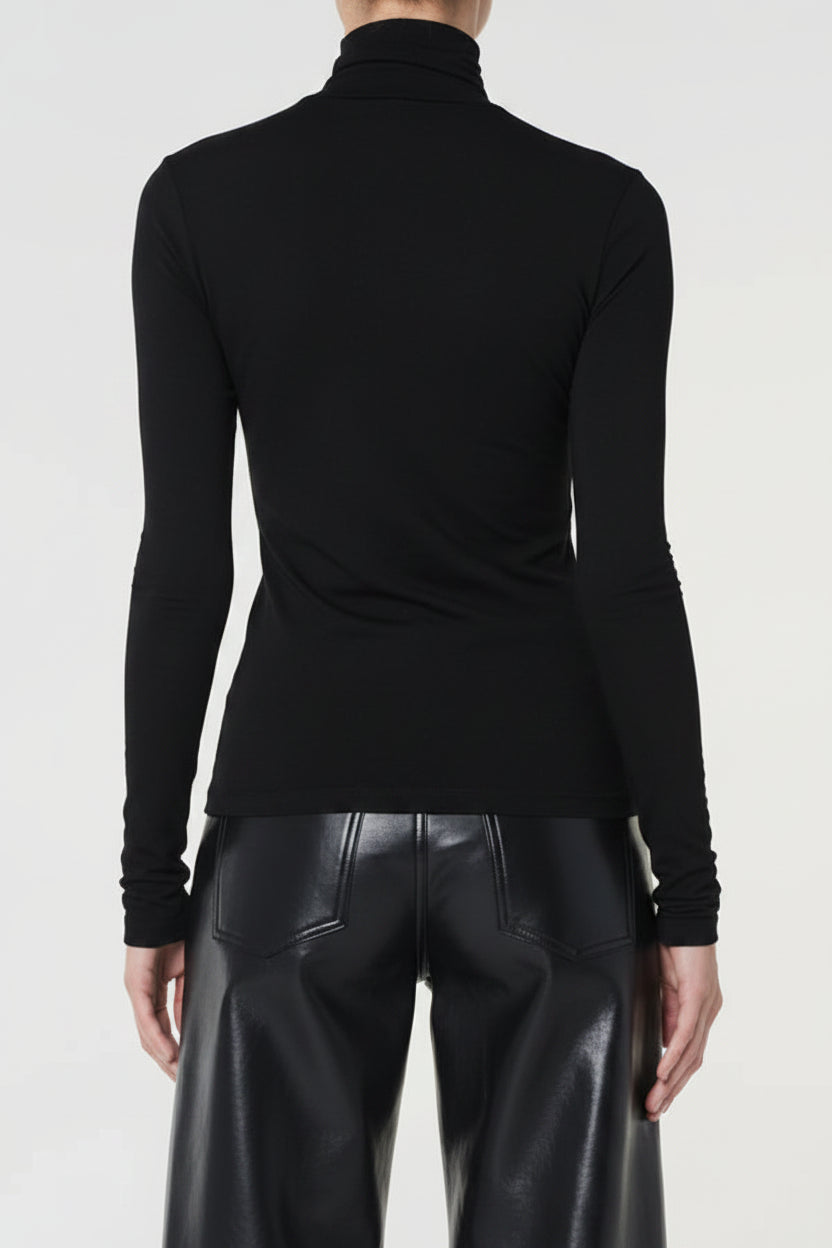 Person wearing a dark gray turtleneck sweater and black leather pants on a white background
