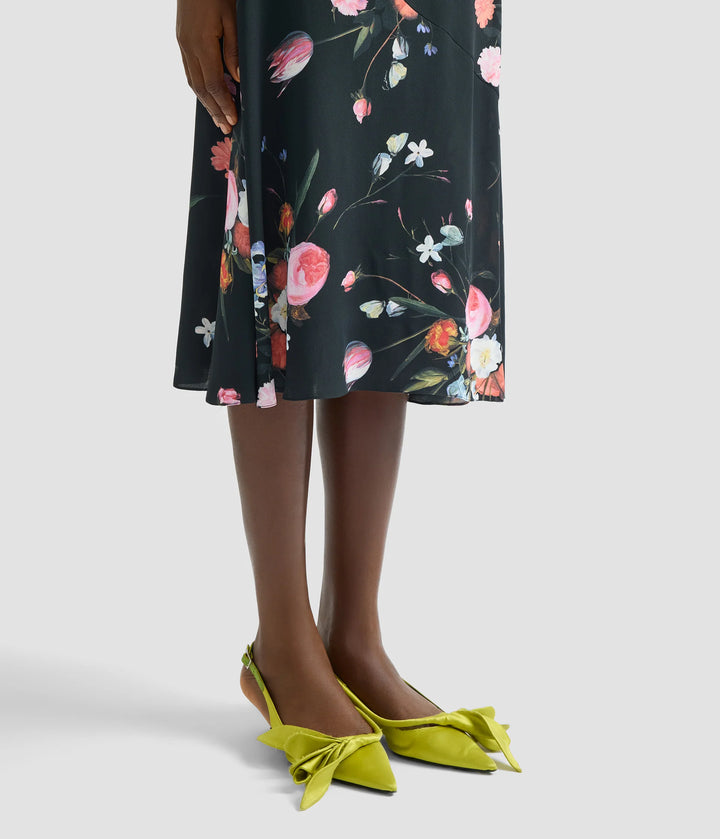 Person wearing a floral dress with green shoes on a white background