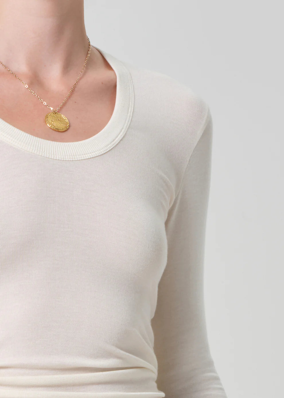 Person wearing a gold necklace with a coin pendant on a plain background