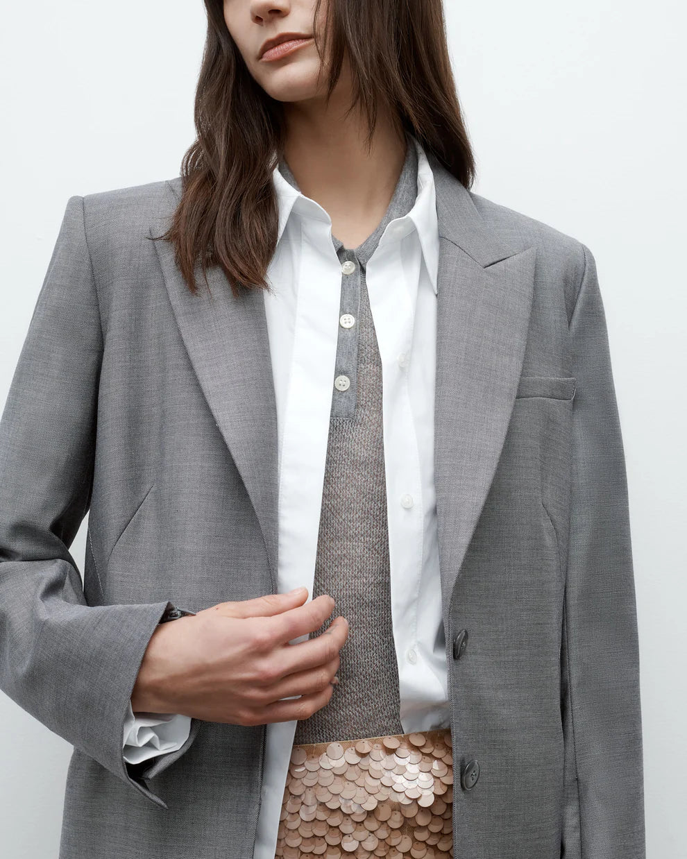 Person wearing a gray blazer over a white shirt and patterned skirt on a plain background