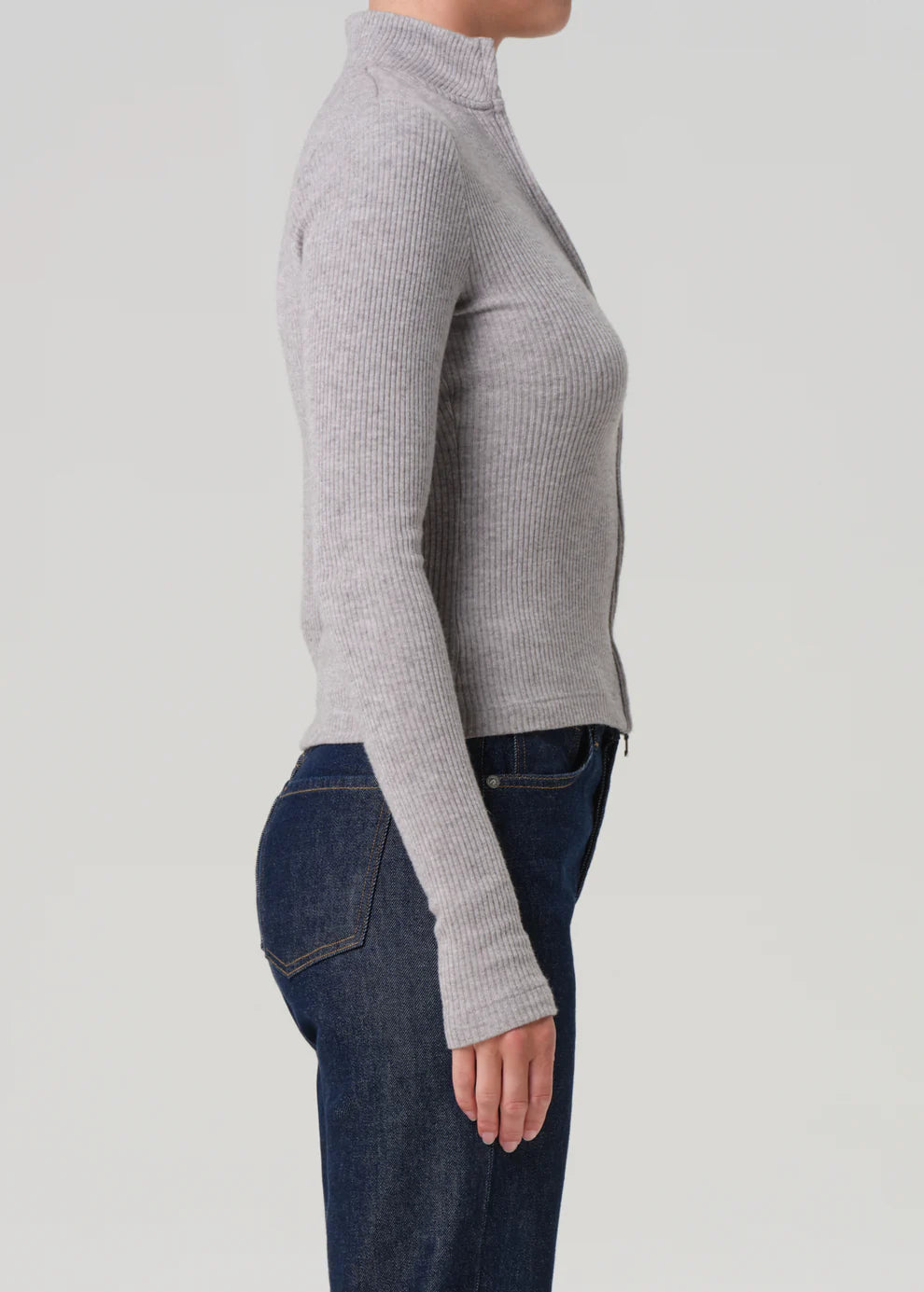 Person wearing a gray ribbed long-sleeve top and blue jeans on a light gray background