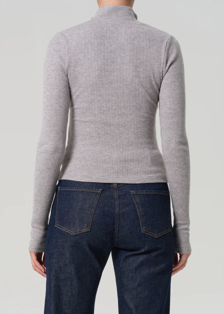 Person wearing a gray ribbed sweater and dark blue jeans on a light gray background