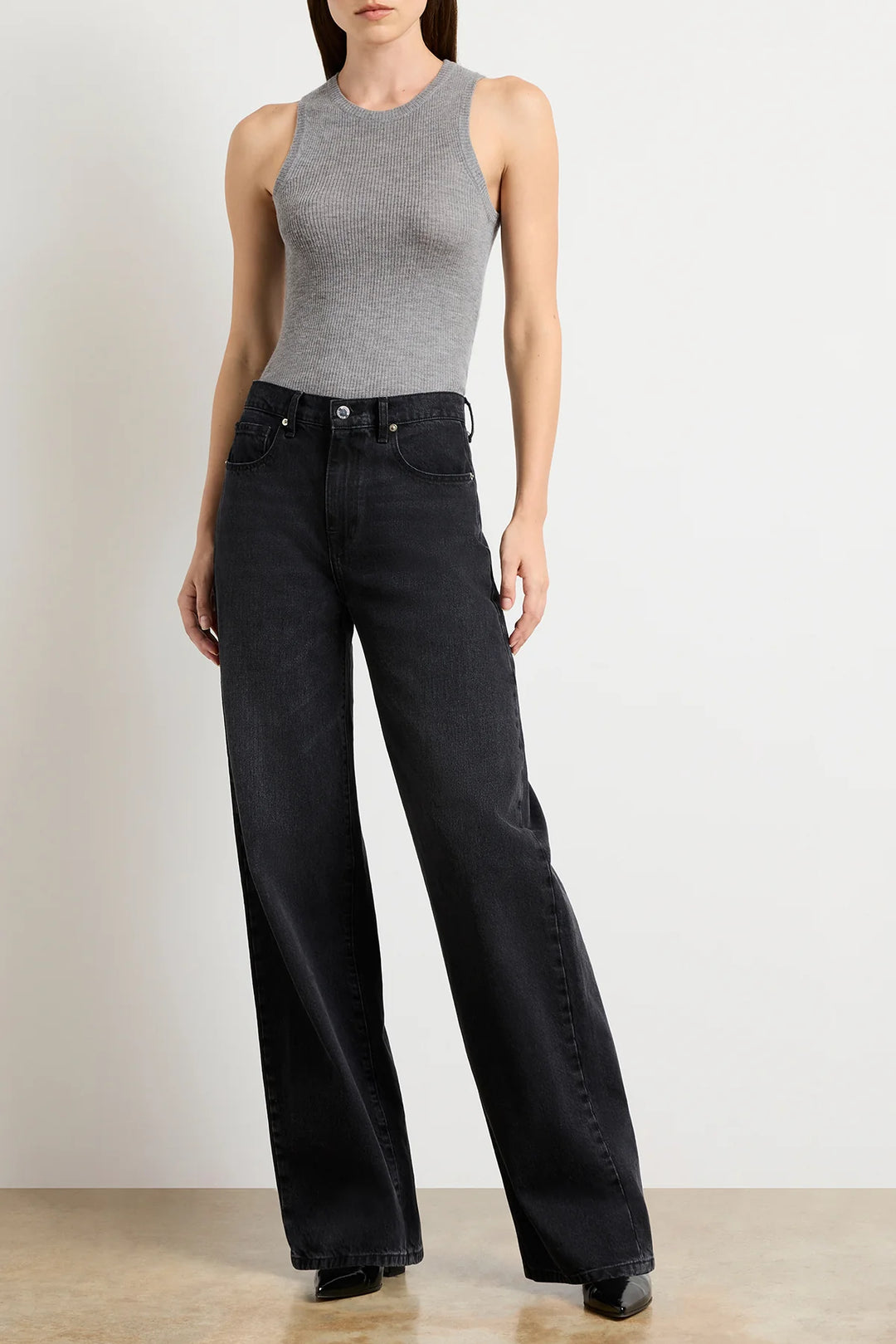 Person wearing a gray sleeveless top and black wide-leg jeans against a plain background