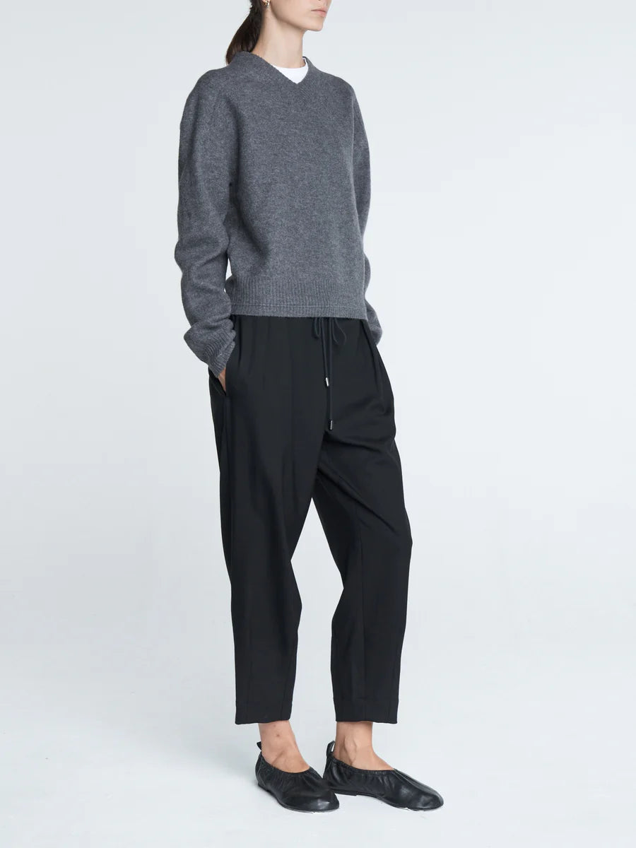 Person wearing a gray sweater and black pants on a white background