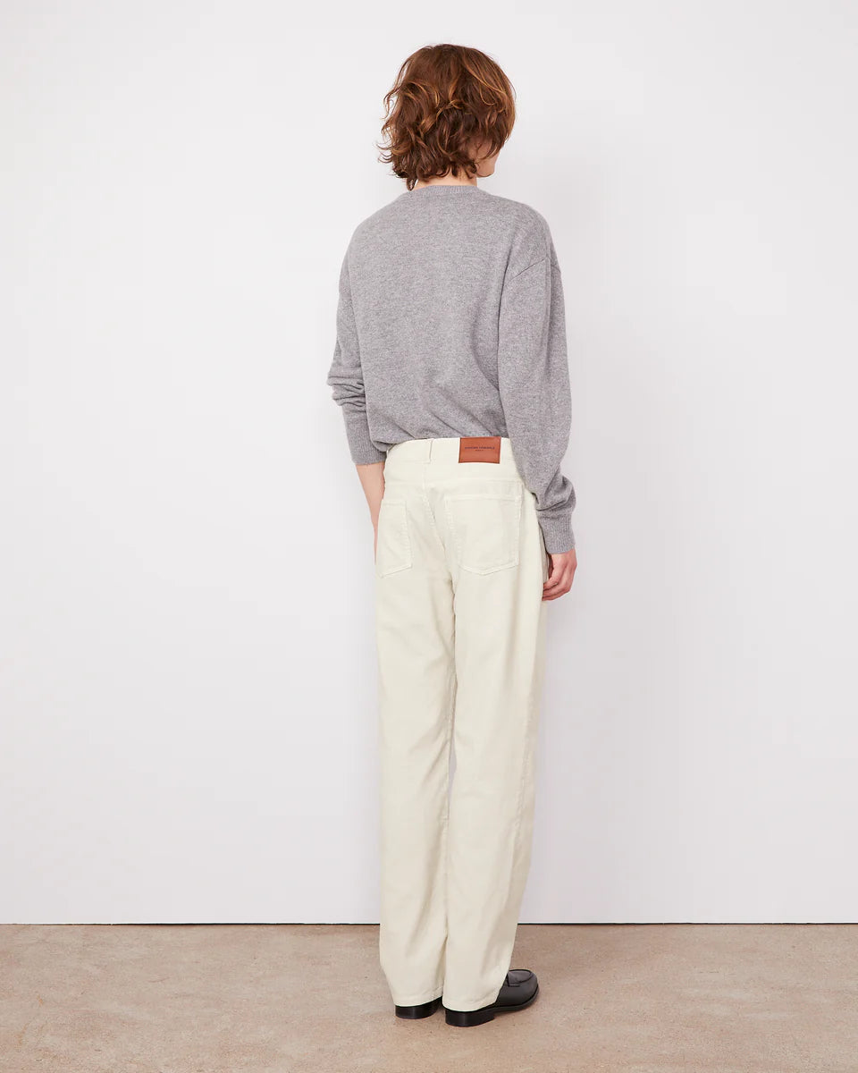Person wearing a gray sweater and white pants standing against a white wall.