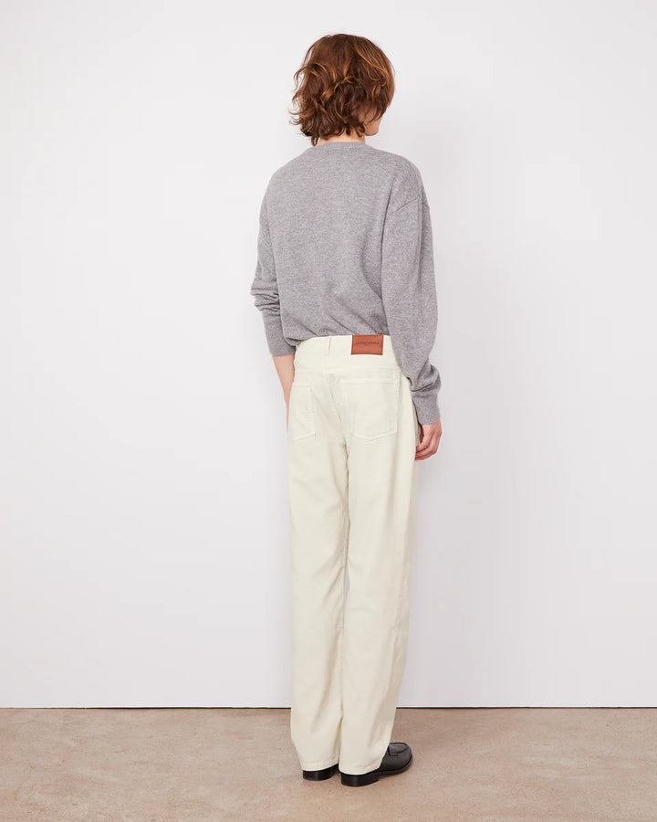 Person wearing a gray sweater and white pants standing against a white wall.