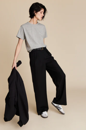 Person wearing a gray t-shirt, black wide-leg pants, and white sneakers on a beige background