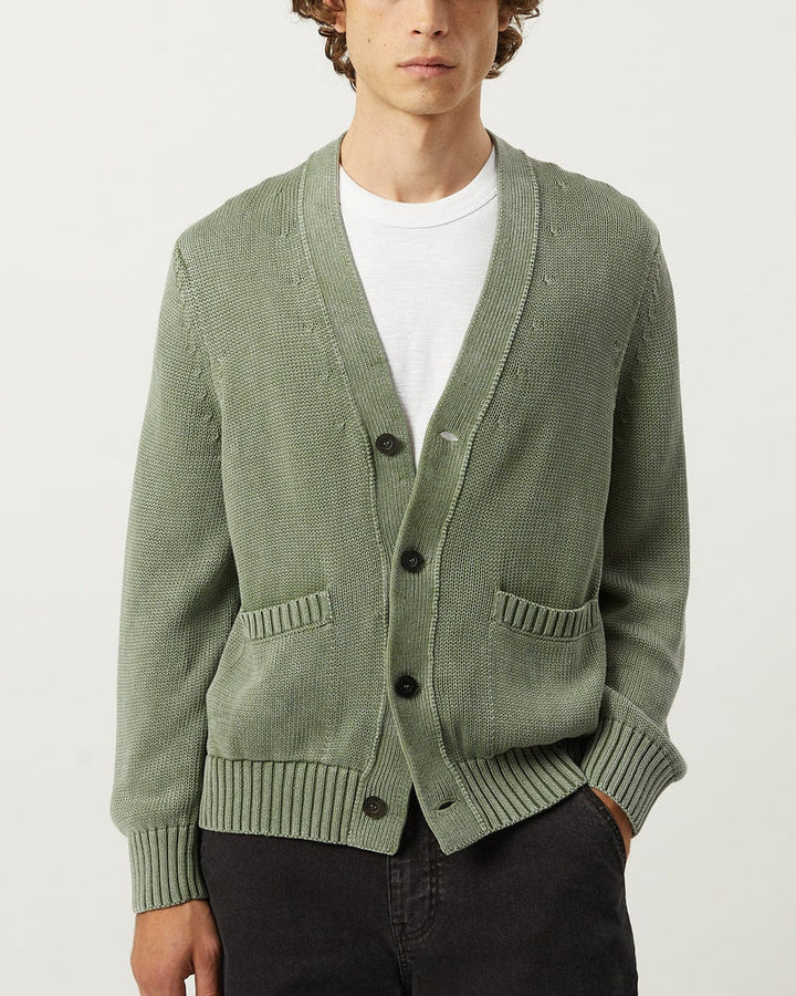 Person wearing a green cardigan over a white shirt on a light gray background