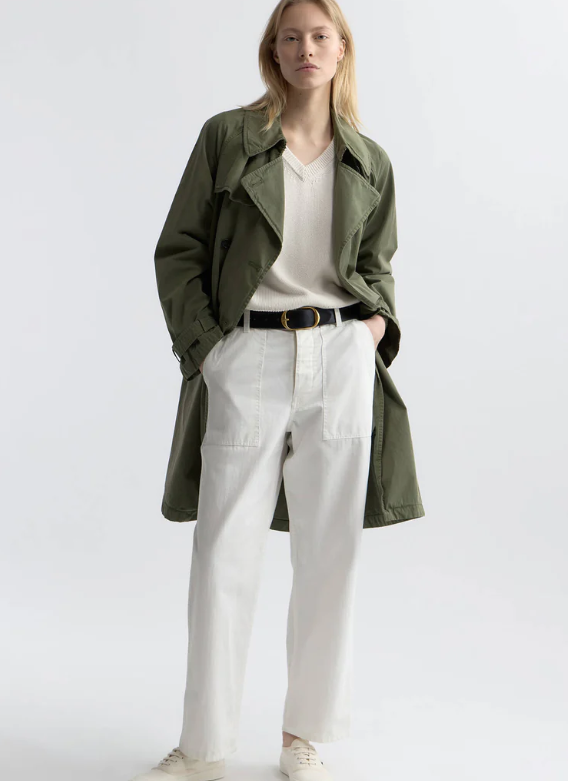 Person wearing a green coat over a white shirt and pants on a plain background