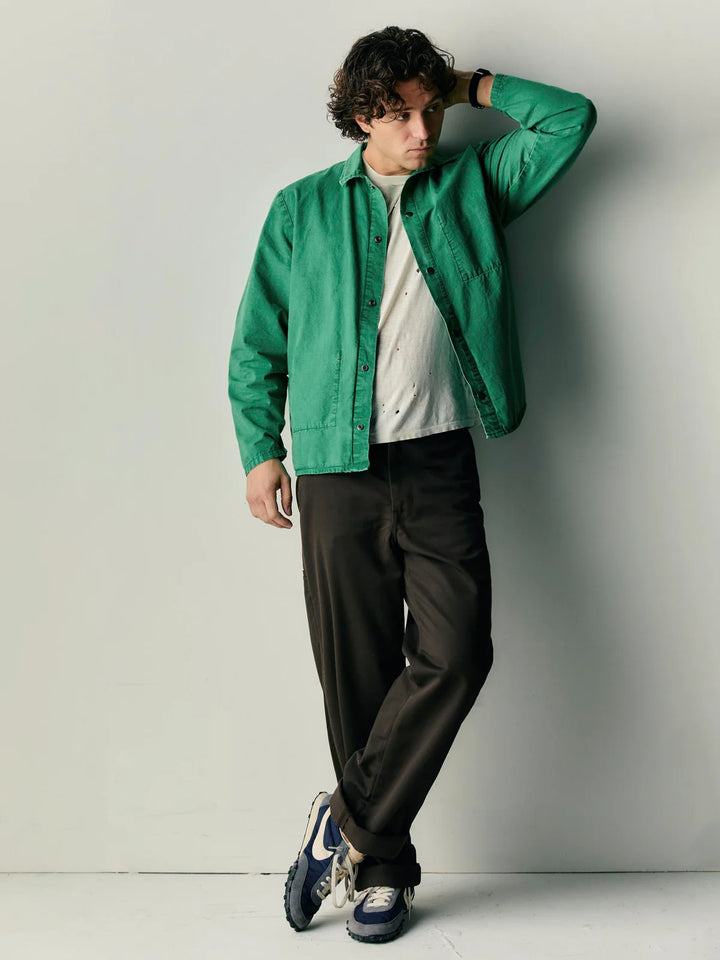 Person wearing a green jacket and dark pants against a plain background