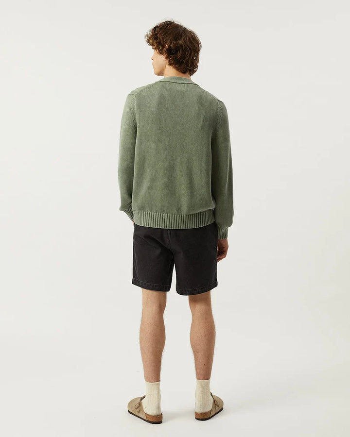 Person wearing a green sweater and black shorts on a white background