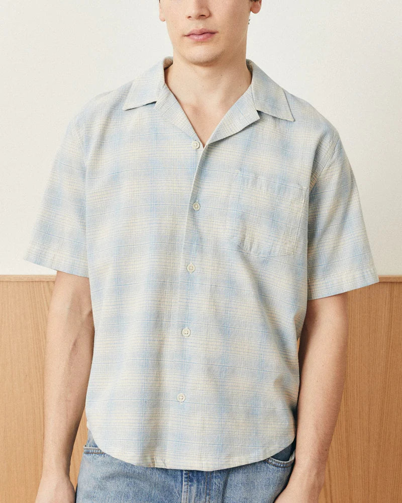Person wearing a light blue and white plaid shirt with a neutral background