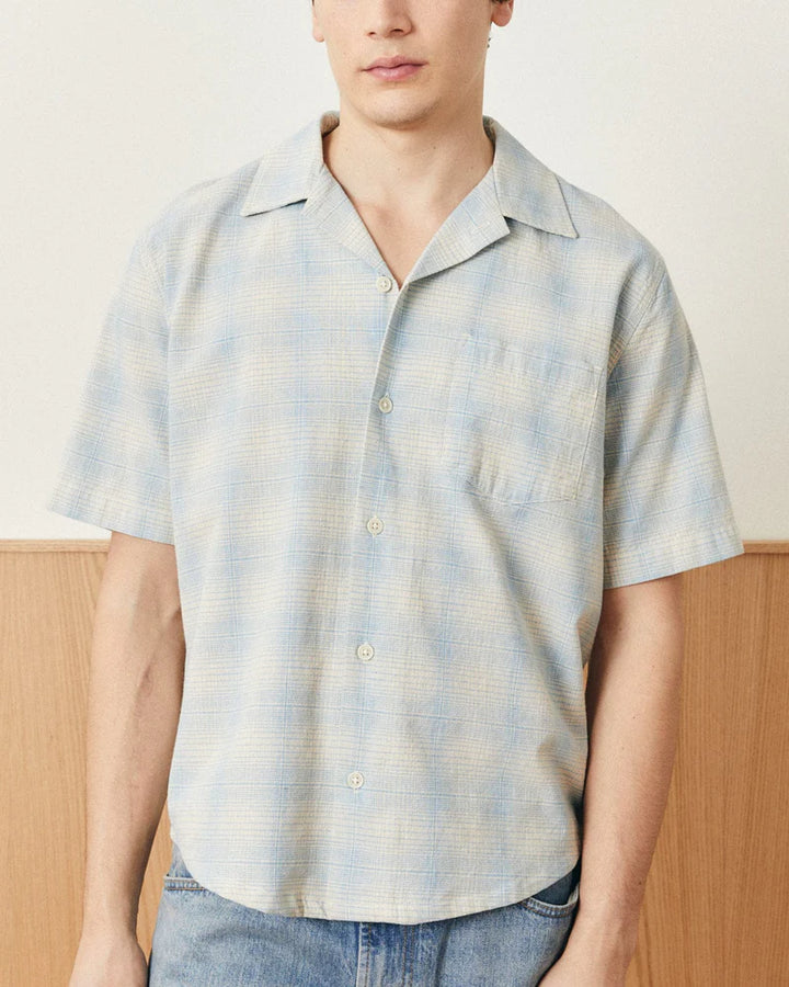Person wearing a light blue and white plaid shirt with a neutral background
