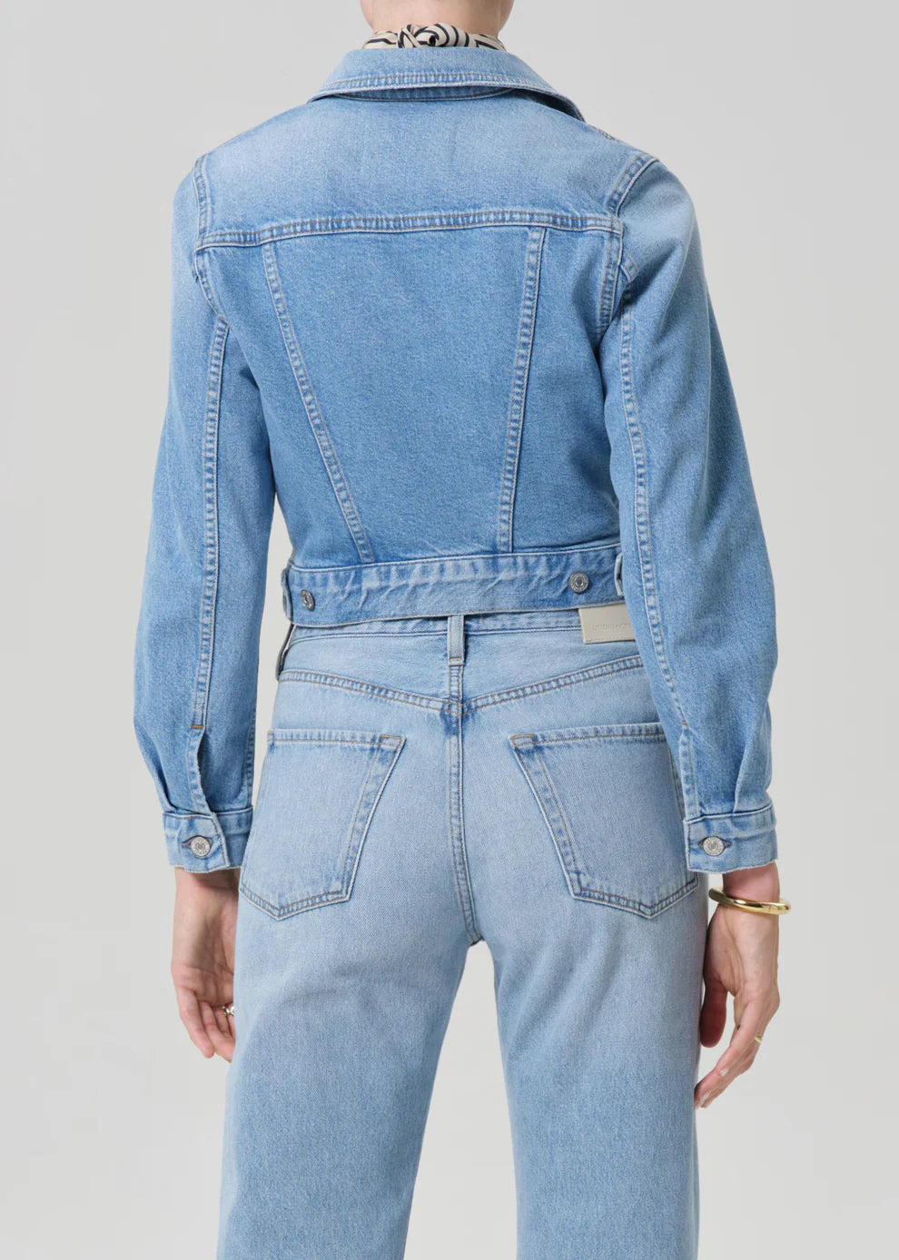 Person wearing a light blue denim jacket and jeans on a plain background
