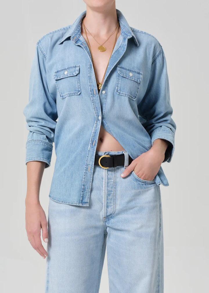 Person wearing a light blue denim shirt and jeans on a plain background