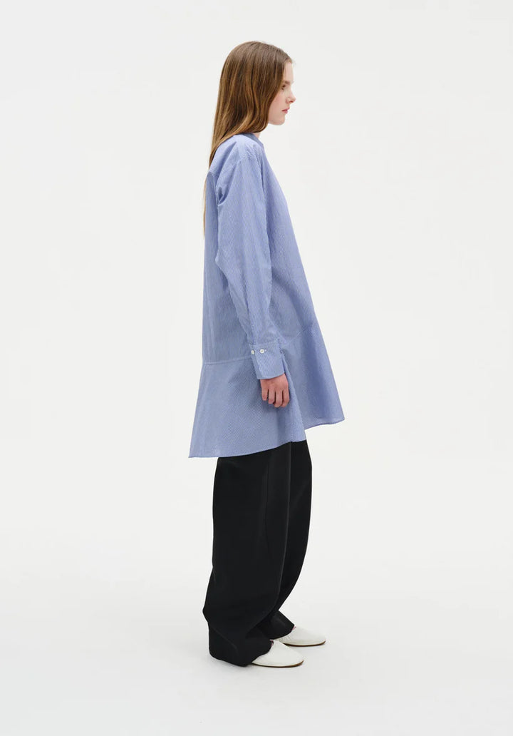 Person wearing a light blue oversized shirt and black pants on a white background