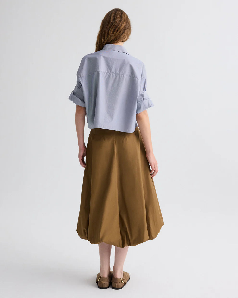 Person wearing a light blue shirt and brown skirt on a white background