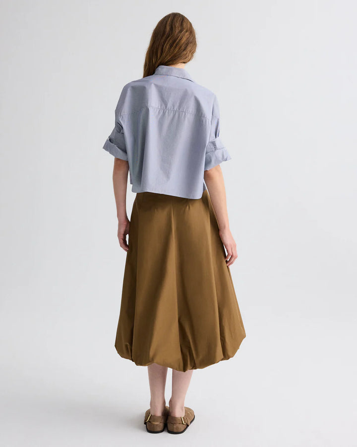 Person wearing a light blue shirt and brown skirt on a white background