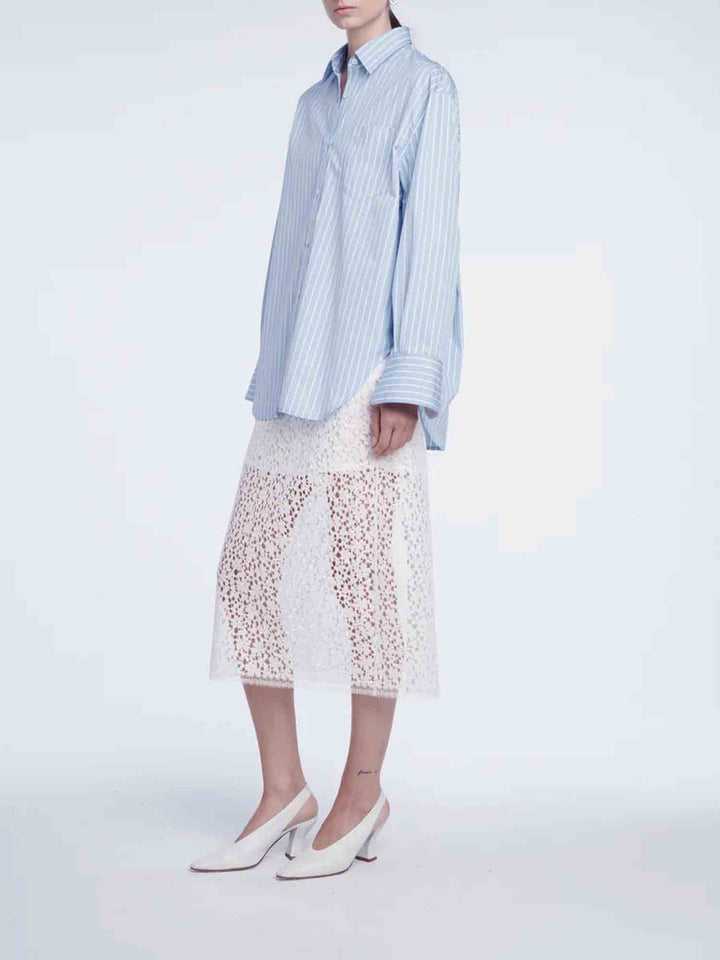Person wearing a light blue striped shirt and white lace skirt on a white background