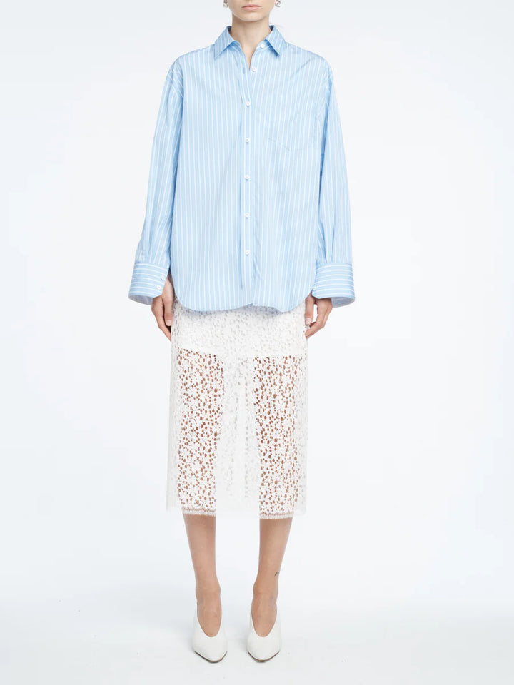 Person wearing a light blue striped shirt and white lace skirt on a white background