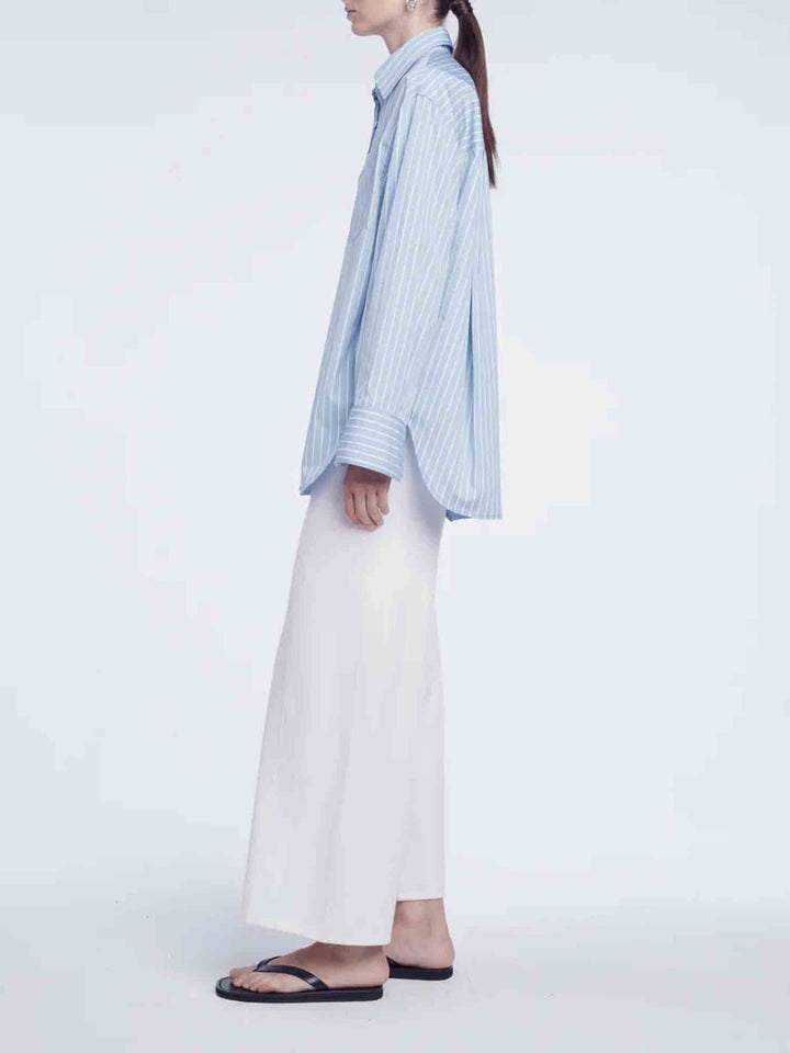 Person wearing a light blue striped shirt and white pants on a plain background