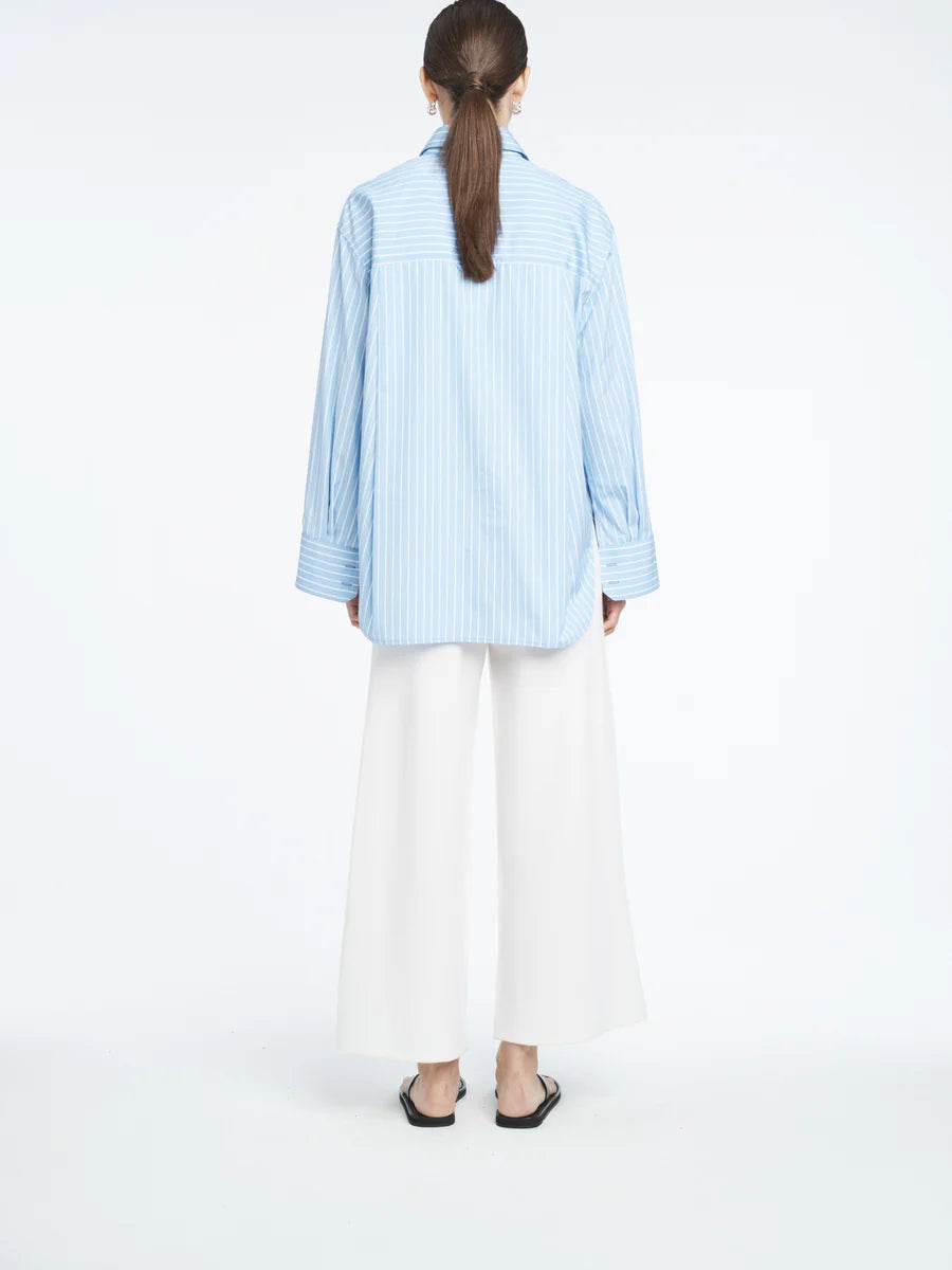 Person wearing a light blue striped shirt and white pants on a white background