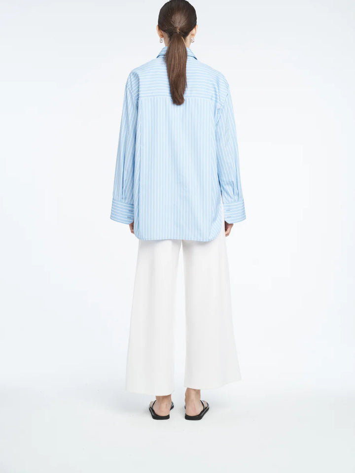 Person wearing a light blue striped shirt and white pants on a white background