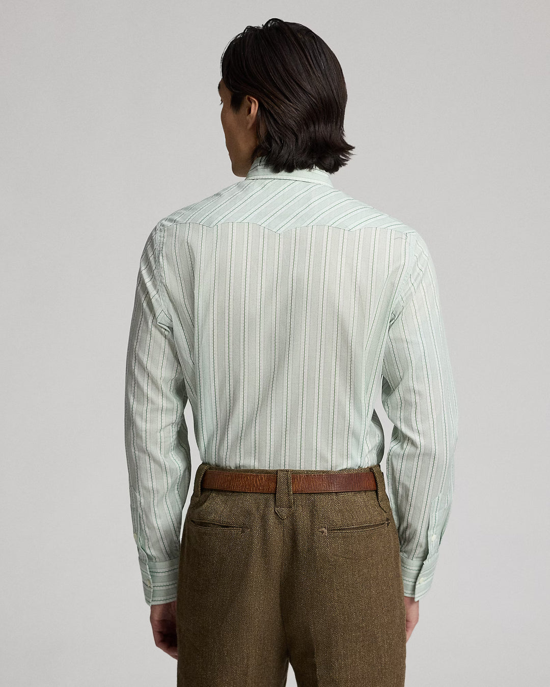 Person wearing a light green striped shirt and brown pants on a gray background