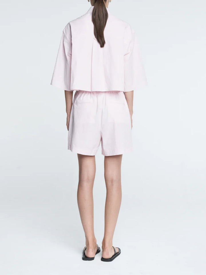 Person wearing a light pink outfit with a jacket and shorts on a white background