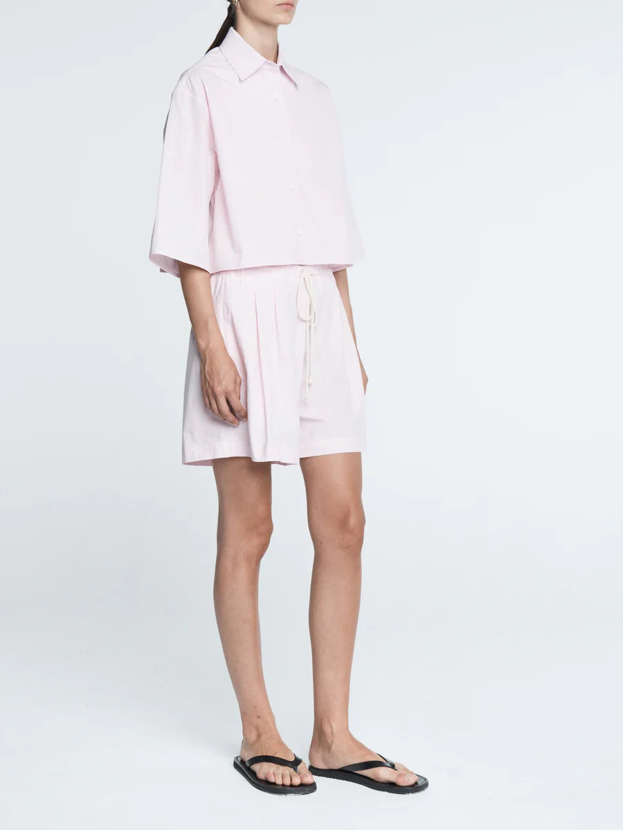 Person wearing a light pink shirt and white shorts on a white background