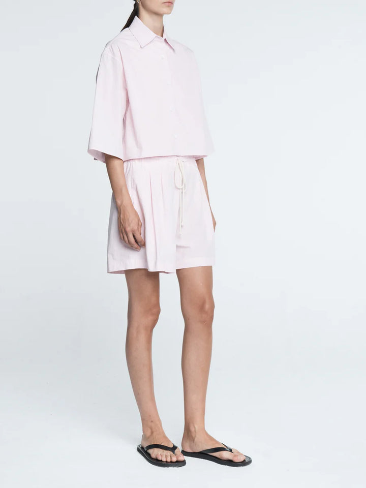 Person wearing a light pink shirt and white shorts on a white background