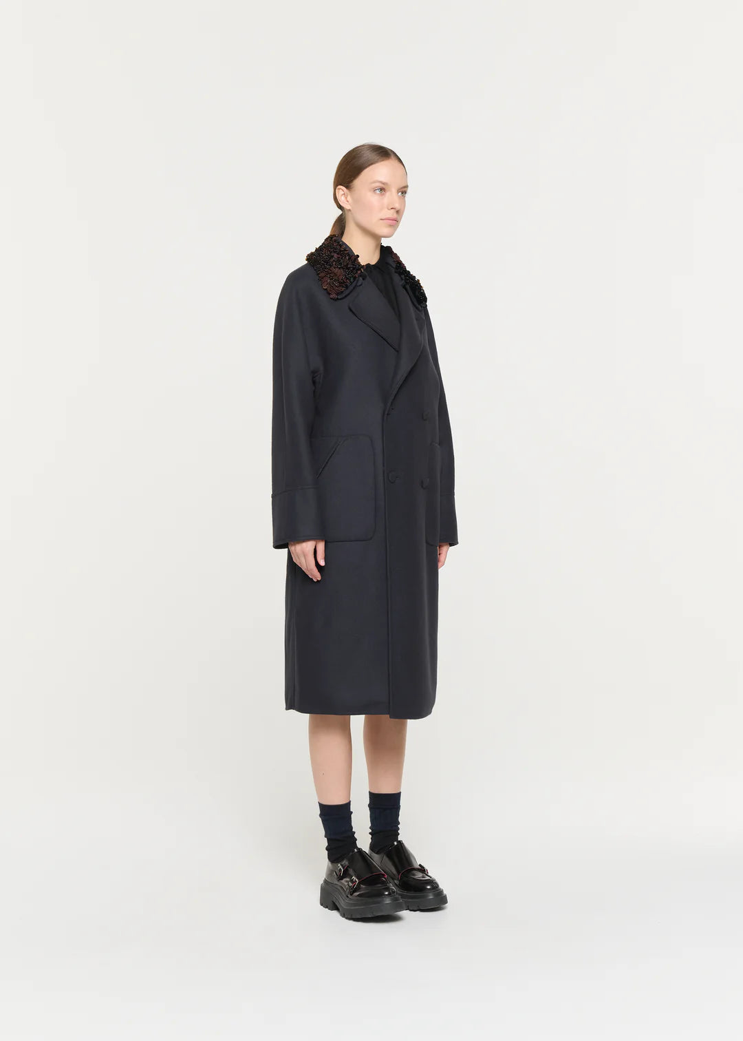 Person wearing a long dark coat on a white background