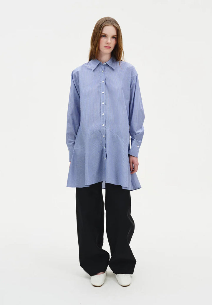 Person wearing a long light blue shirt and black pants on a white background