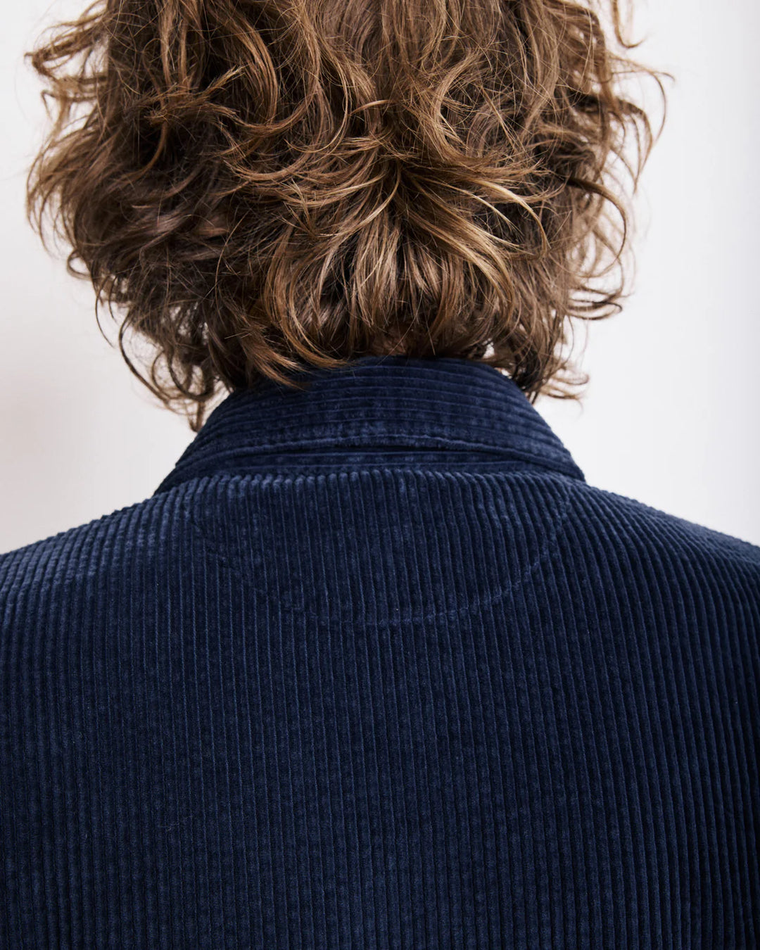 Person wearing a navy blue corduroy jacket with a neutral background