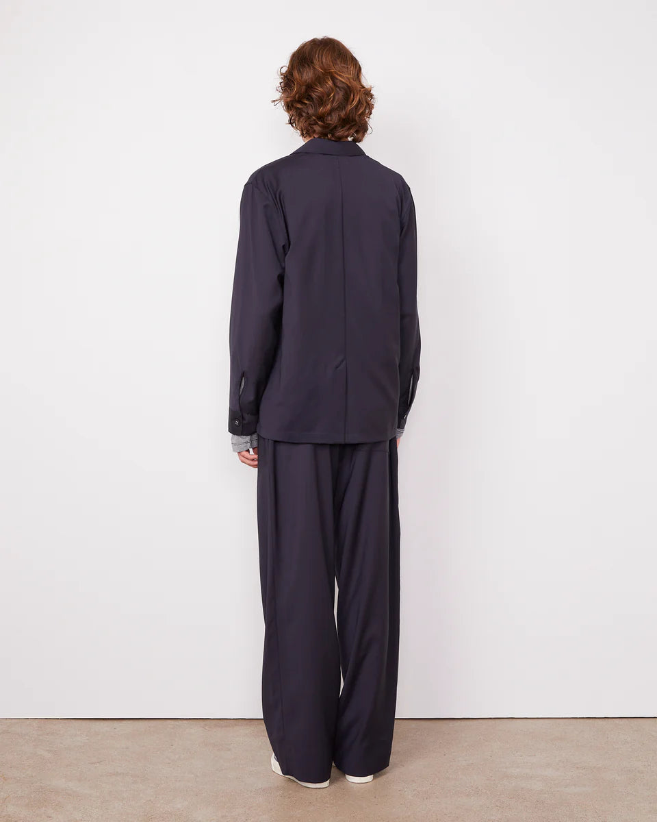 Person wearing a navy blue outfit standing against a white wall.