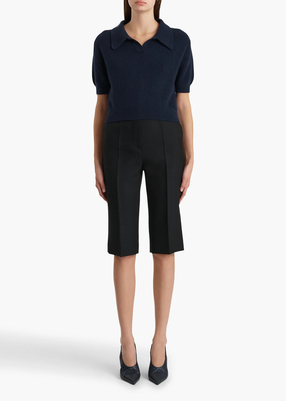 Person wearing a navy blue polo shirt and black capri pants on a white background