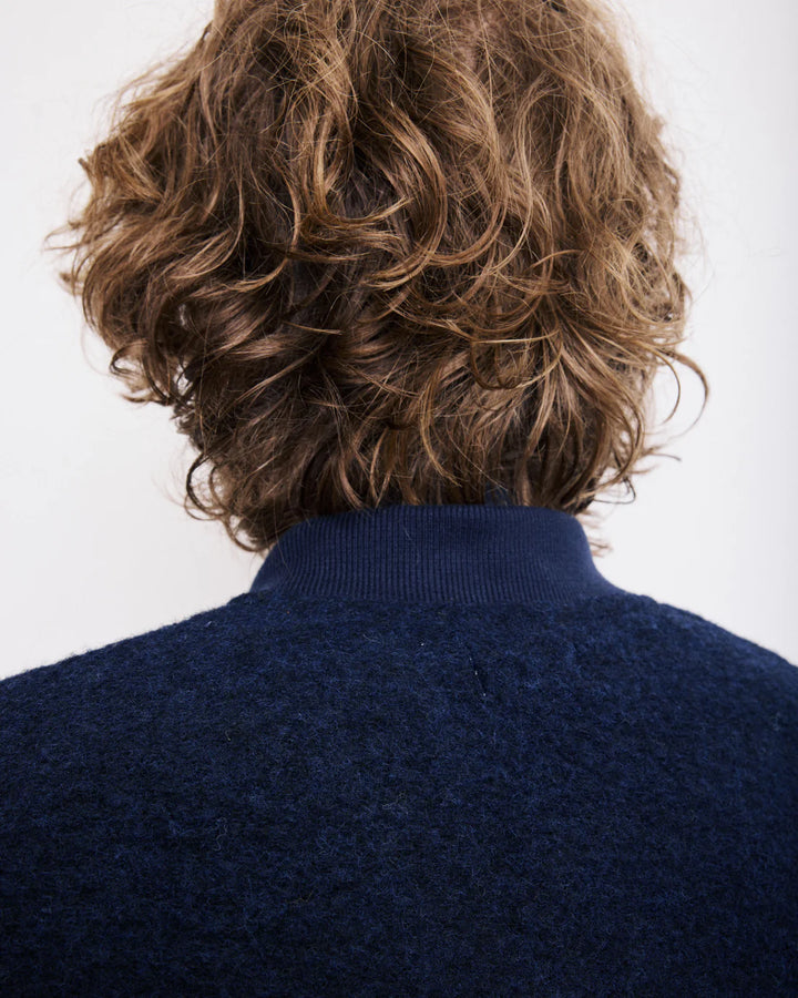 Person wearing a navy blue sweater with wavy brown hair on a white background