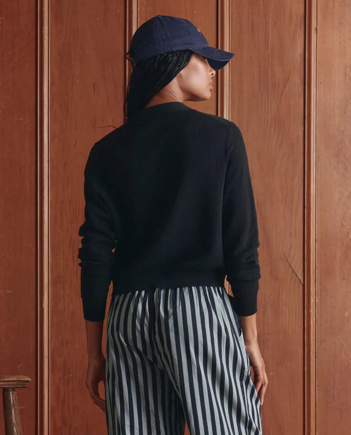 Person wearing a navy cap and black sweater with striped pants against a wooden door.