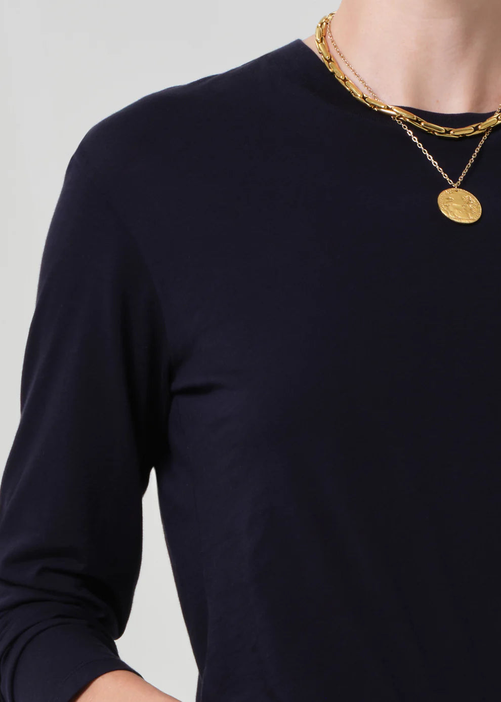 Person wearing a navy long-sleeve shirt with gold necklaces on a light gray background