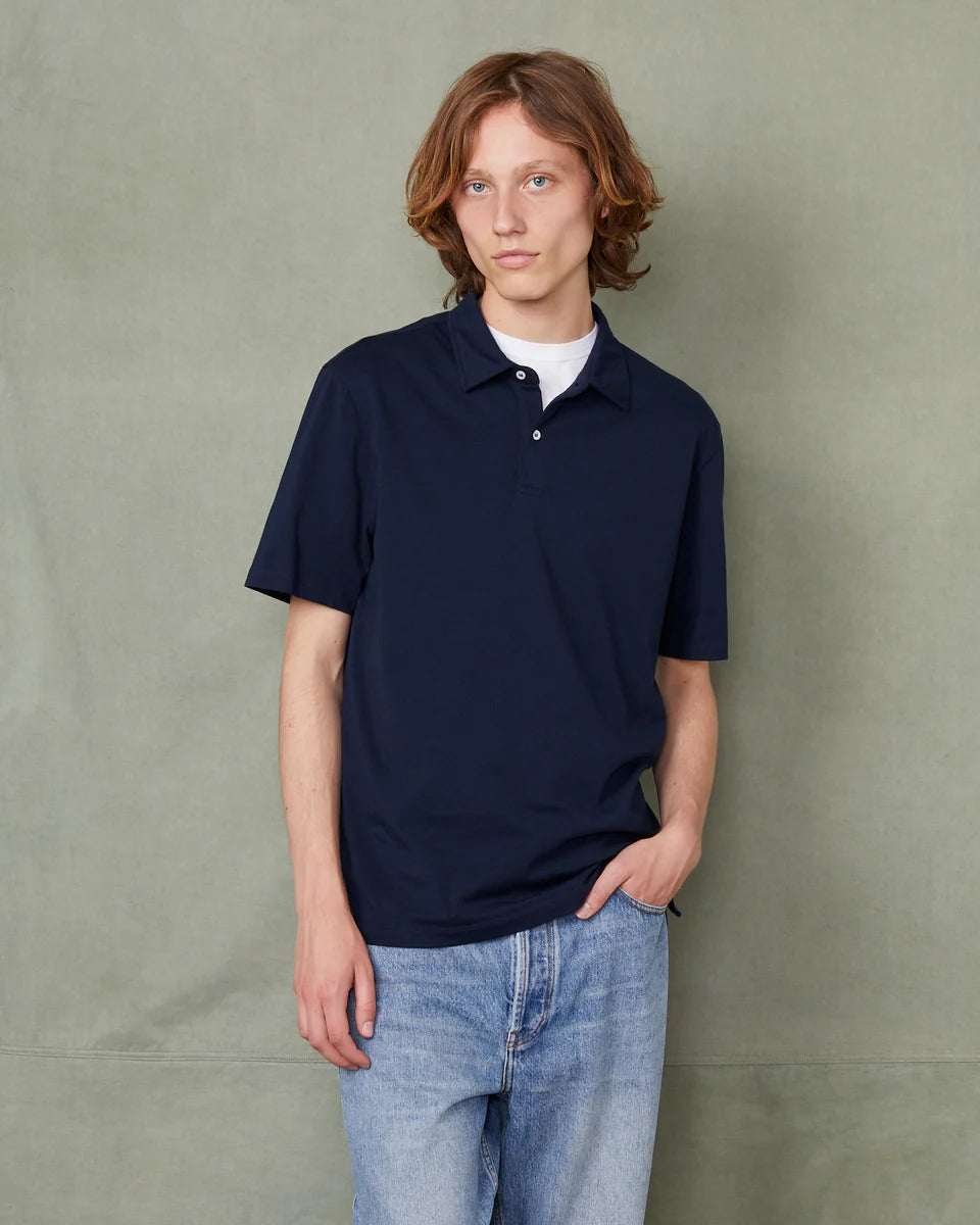 Person wearing a navy polo shirt and light blue jeans against a plain background