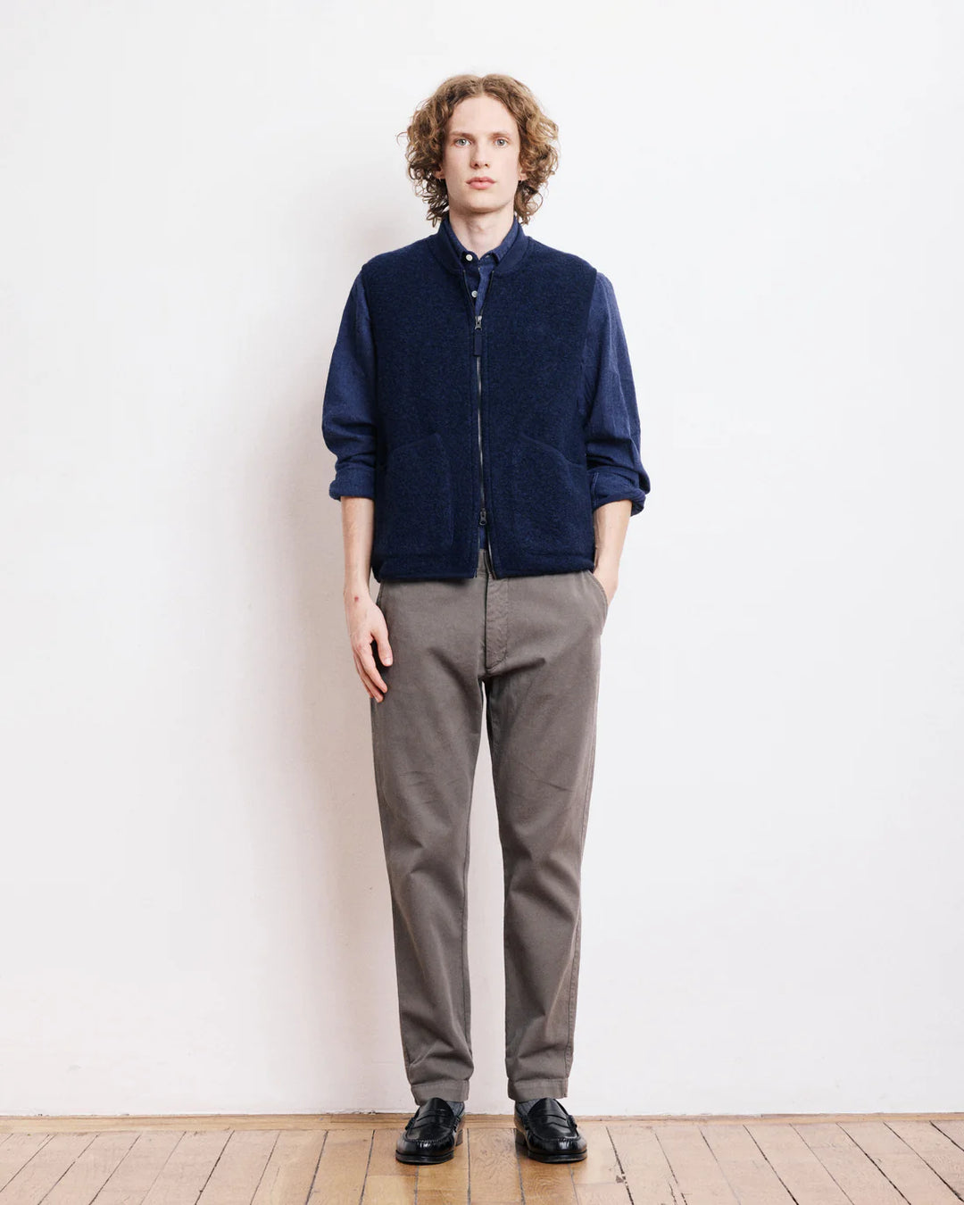 Person wearing a navy sweater and gray pants against a white wall.