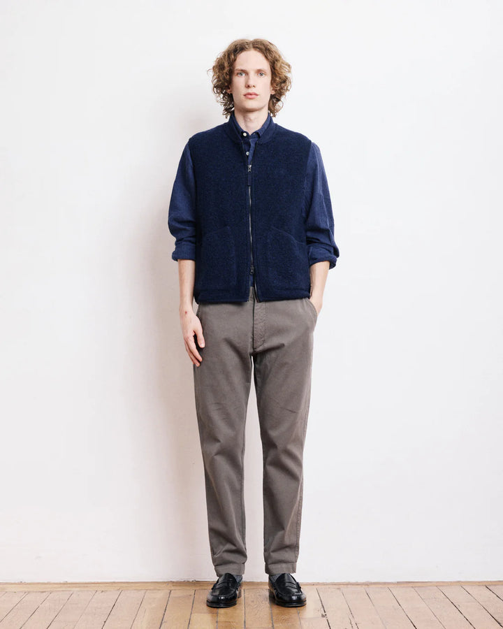 Person wearing a navy sweater and gray pants against a white wall.