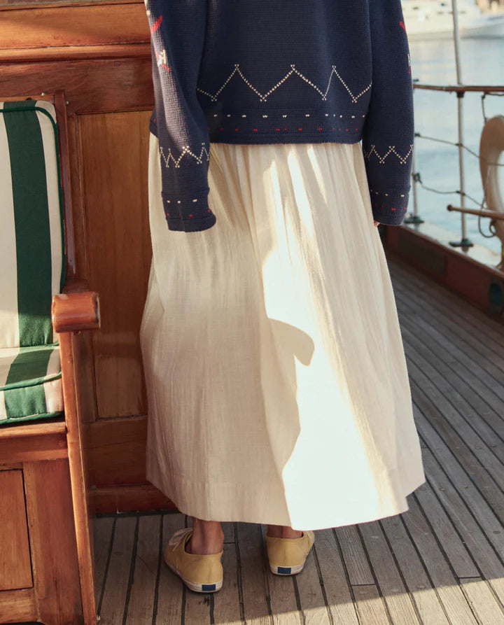 Person wearing a navy sweater with a pattern and a beige skirt on a boat deck.