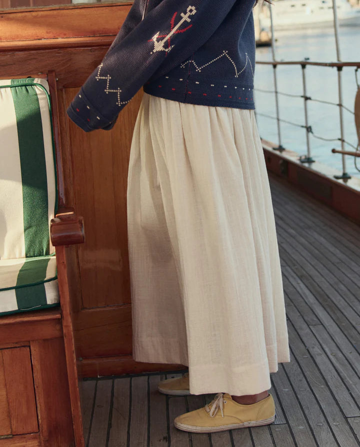 Person wearing a navy sweater with anchor design and beige skirt on a boat deck.