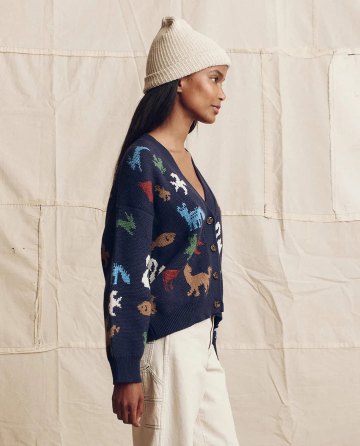 Person wearing a navy sweater with colorful dog patterns against a beige textured wall.