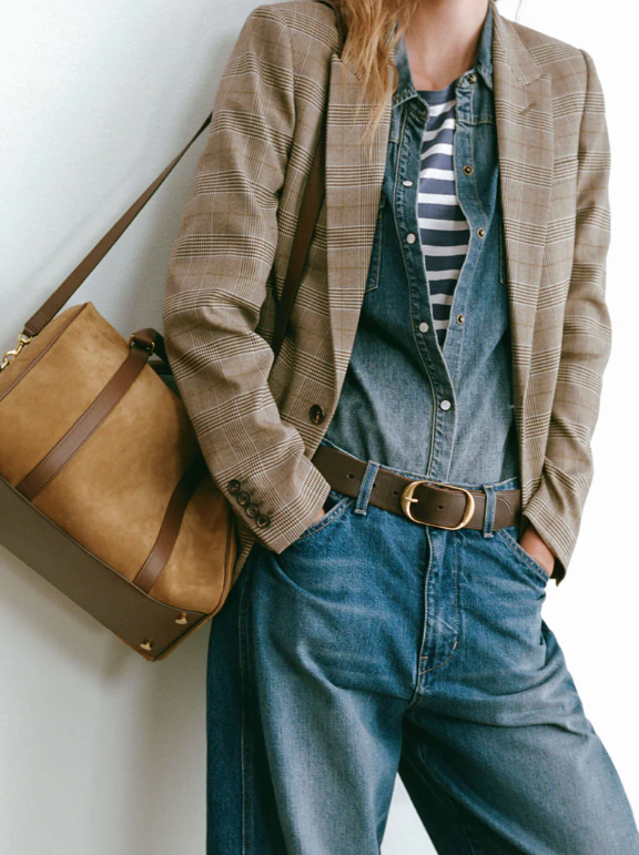 Person wearing a plaid blazer, denim overalls, and striped shirt with a brown leather bag.