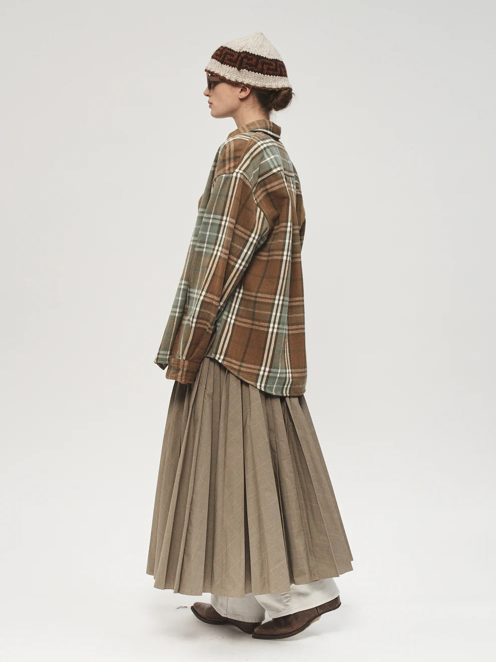 Person wearing a plaid shirt and pleated skirt with a hat on a white background