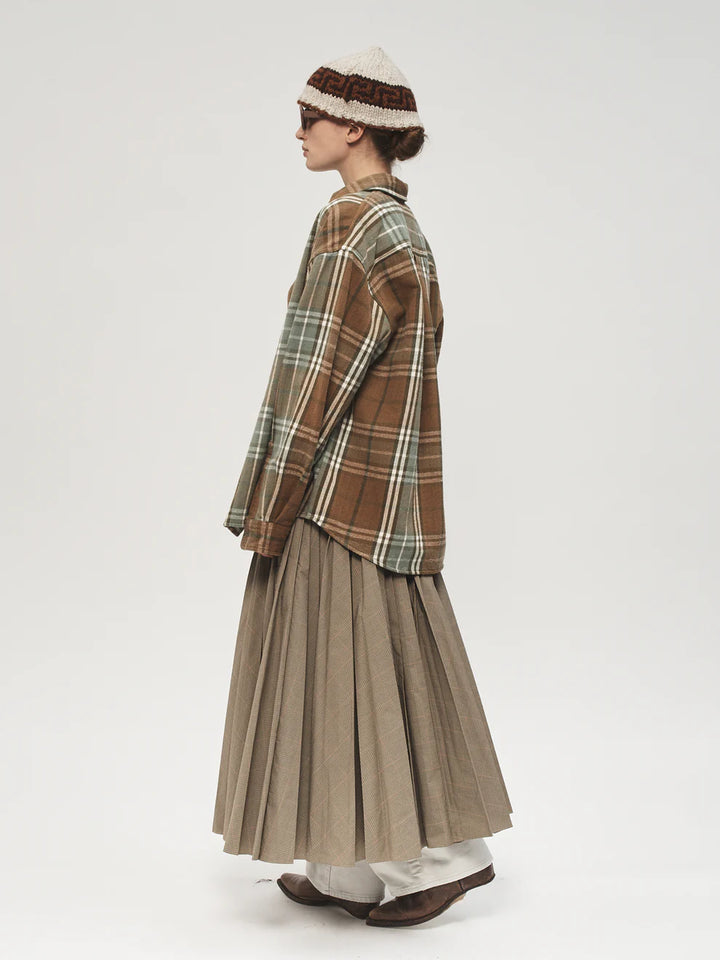 Person wearing a plaid shirt and pleated skirt with a hat on a white background